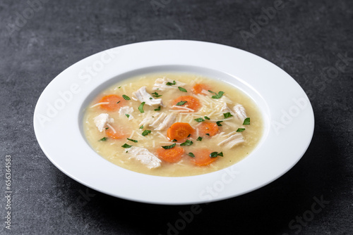 Chicken soup with vegetables on black slate background