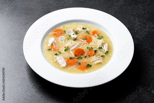 Chicken soup with vegetables on black slate background