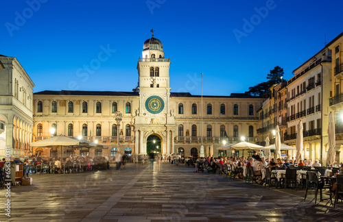 Padua, Italy - October 1, 2023: Piazza dei Signori or Piazza della Signoria in the evening. The square is dominated by the famous Clock Tower. People sitting at the tables in the bar or walking around