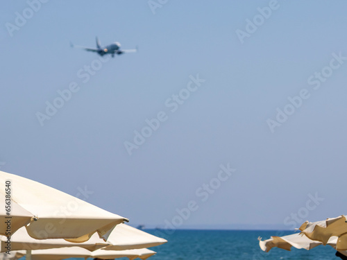 Beach umbrellas in front of blue sea and sky with blurred flying airplane, Cyprus