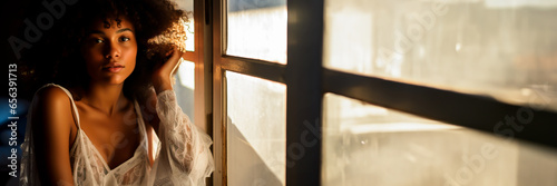 Beauty or fashion photography of a young woman sitting in a window in evening light. Urban feel. Concept of fashion or beauty commercials or ads. Shallow field of view and copy space.