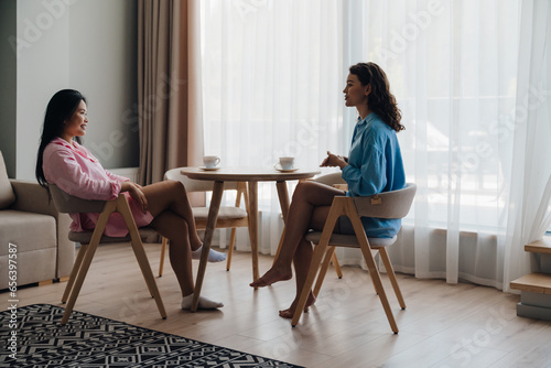 Two beautiful women drinking coffee and talking while sitting in living room