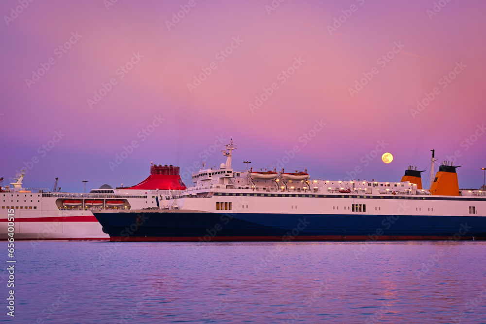 Two ferries moored by pier during colorful sunset and moonrise in port