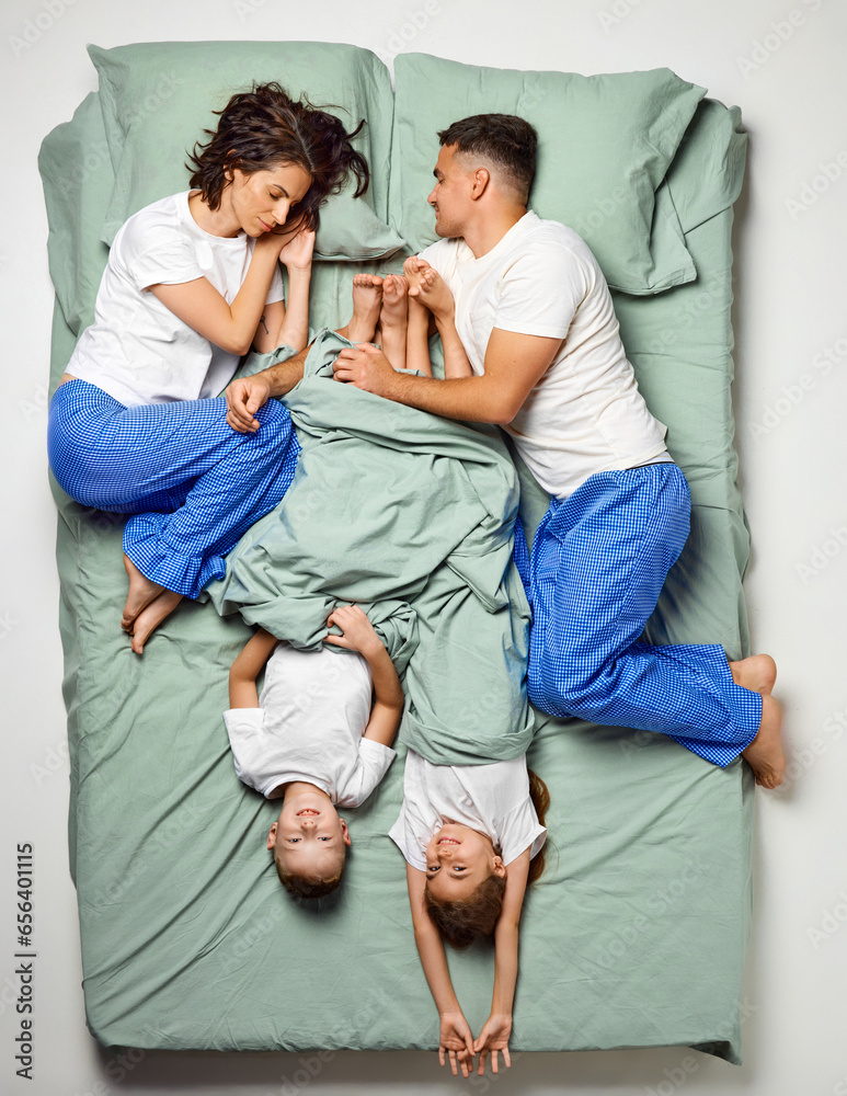 Top view portrait of people covered with blanket lying in bed. Children