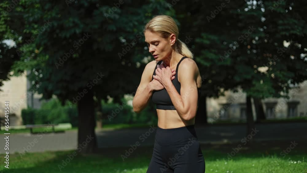 Tired woman in black sport attire having problems with breath because of chest pain after morning run. Fitness lady with blond hair standing at sunny park and suffering from asthma or heart attack. Tired woman in black sport attire having problems with breath because of chest pain after morning run. Fitness lady with blond hair standing at sunny park and suffering from asthma or heart attack.