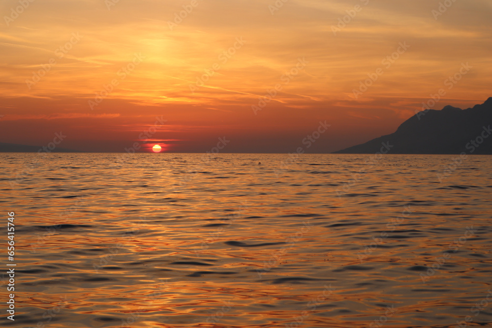 Obraz premium Sunset over the sea, orange sun in the clouds on the horizon, sea coast of Croatia, Dalmatia, Brela