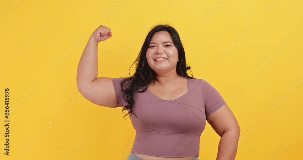 A chubby Asian woman wearing exercise clothes is showing off her physical strength on a yellow background. A chubby Asian woman wearing exercise clothes is showing off her physical strength on a yellow background.