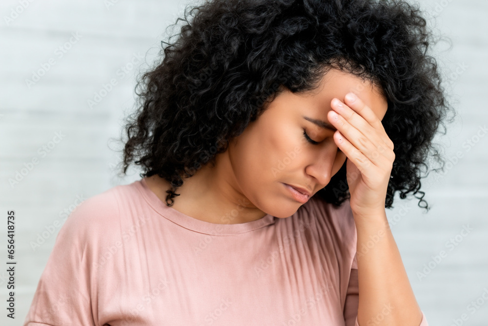 Woman with severe headache wearing pink blouse and black curly medium length hair Woman with severe headache wearing pink blouse and black curly medium length hair