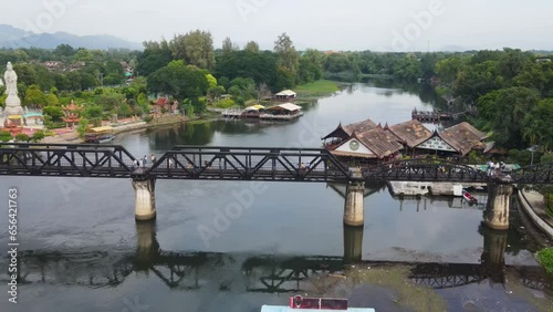 A scenic footage with a drone of this super lovely River Kwai Memorial Bridge; sliding to the left revealing a temple, communities and resorts then the river, Kanchanaburi, Thailand photo