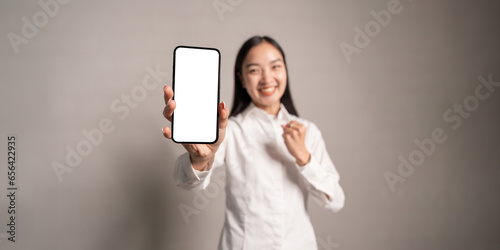 Joyful asian woman, showing her smartphone with empty white mockup screen, rejoices in success, looks at camera, make YES gesture
