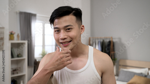 smiling Korean male looking at camera like mirror satisfied with his perfect facial skin while getting ready for the day at home.