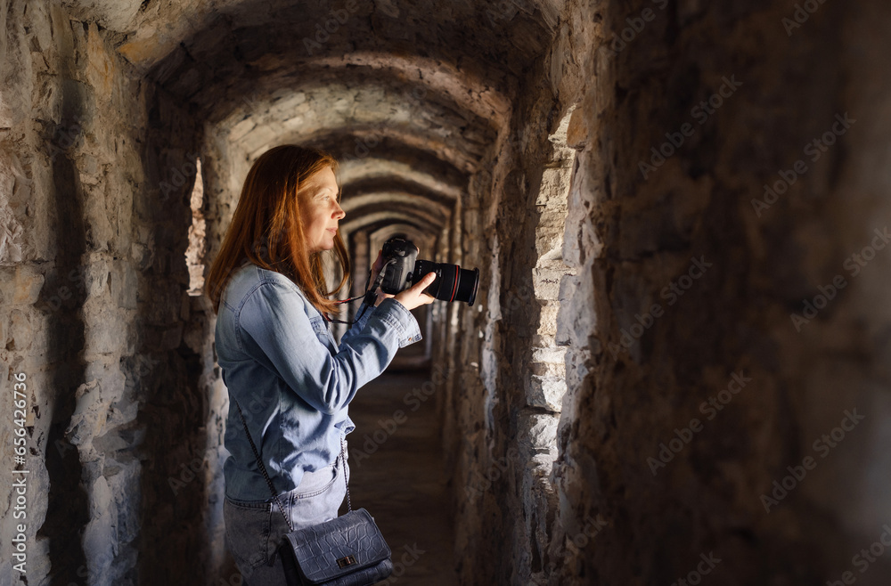 Woman taking pictures in old tunnel, looking in window and walking through. Female visiting castle. Traveling in ancient building 