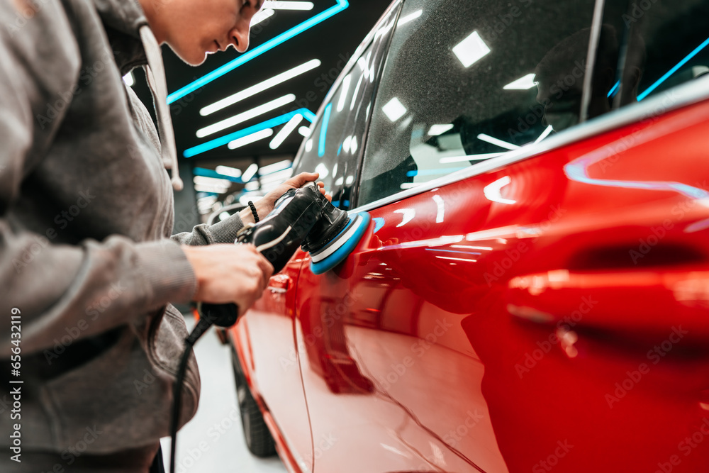 Professional vehicle polishing and detailing service in a modern car workshop. Brightly lit workspace with large led lights. High quality car valeting concept.