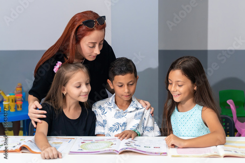 Teacher and school student children studying at desk in educational classroom  writing in notebook  reading book. Group of diverse classmates learning. Academic Concept.