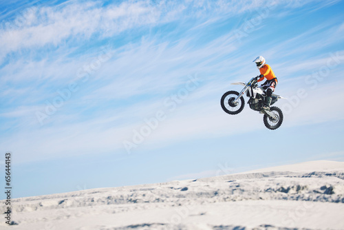 Motorcycle, desert and jump for sports in race, adrenaline and training for fitness in competition. Athlete, sky and mockup for freedom, driving and dirtbike in outdoor for stunt or performance photo