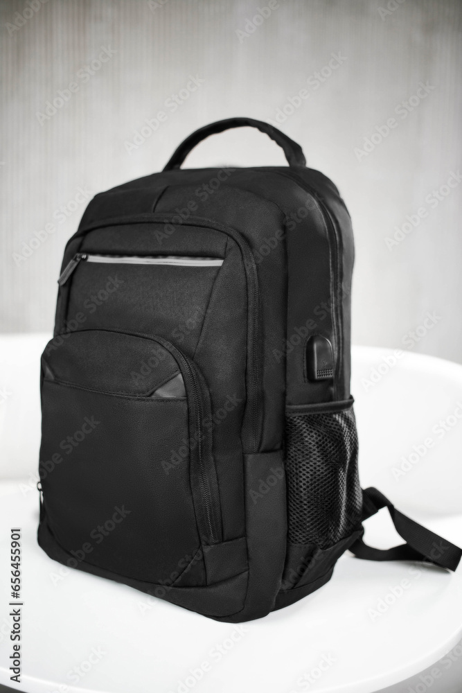 Naklejka premium A black backpack with pockets in the front stands on a white table