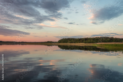 Obraz na płótnie Scenery of nature of Braslav lakes. Beautiful sunset on Snudy lake, the sky is overcast with small clouds. The sky is reflected from the surface of the lake water. w salonie