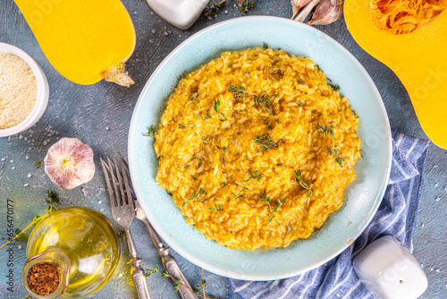 Delicious homemade cheesy puff pumpkin risotto with parmesan cheese and thyme, with ingredients and spices on blue concrete table