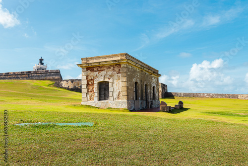 old stone structure in the middle of a green field from el morro with the san felipe castle behind in puerto rico san juan photo