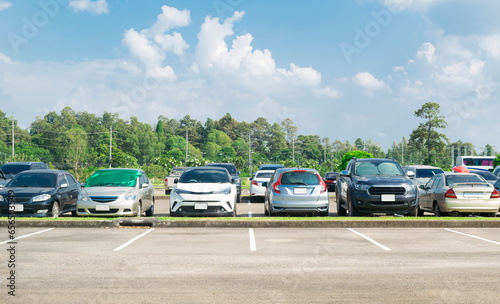 Fototapeta Naklejka Na Ścianę i Meble -  Cars parking in asphalt parking lot in a row with blue sky background. Outdoor parking lot with fresh ozone, green nature environment of transportation and technology concept