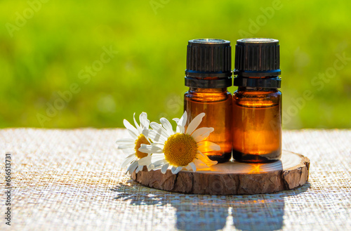 Chamomile essential oil. Dark glass bottle with essential oil and chamomile flowers on the table