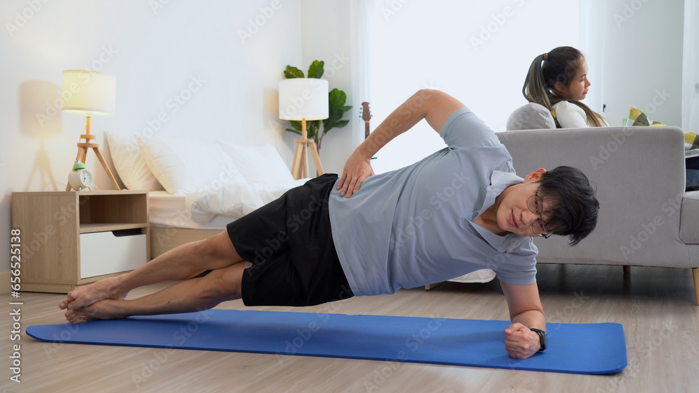 happy asian young man doing exercise and watching tutorial on laptop with mat in living room at home. Asia male doing workout woman watch television or tv . couple lifestyle at home . happy asian young man doing exercise and watching tutorial on laptop with mat in living room at home. Asia male doing workout woman watch television or tv . couple lifestyle at home .