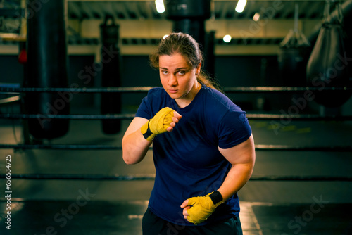 portrait focused Boxer girl in yellow boxing bandages standing in a boxing stance on a dark background in a gym before a fight © Guys Who Shoot