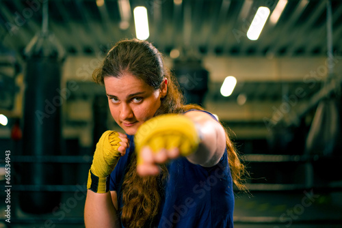 portrait focused Boxer girl in yellow boxing bandages standing in a boxing stance on a dark background in a gym before a fight