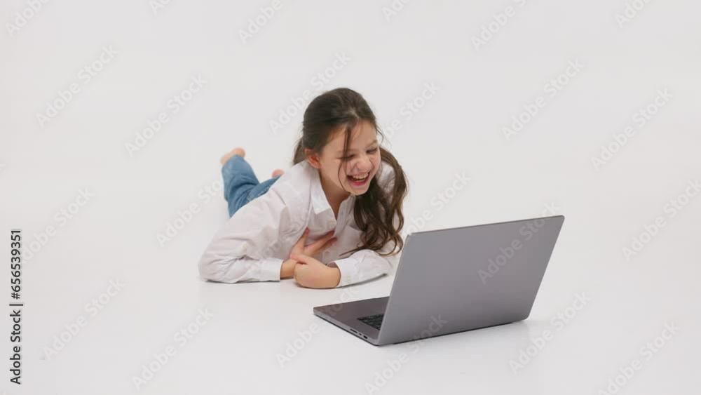 The concept of childish, sincere emotions. A little girl lies on the floor against a light background and watches a movie. Happy childhood concept The concept of childish, sincere emotions. A little girl lies on the floor against a light background and watches a movie. Happy childhood concept