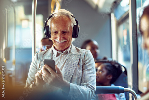 Senior businessman using his phone while going to work on the bus