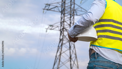A male power engineer in a white helmet checks a power line using data from electrical sensors on a tablet. High voltage electrical lines at sunset. Distribution and supply of electricity