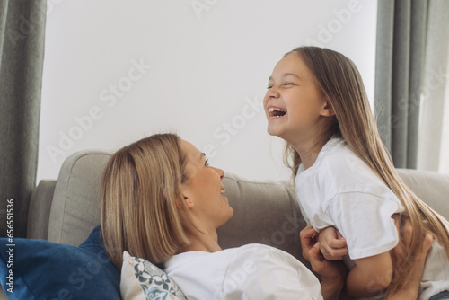 Mother and daughter having fun spending leisure time together at home playing and cuddling.