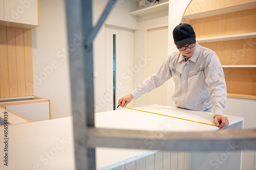 Home renovation or House remodeling concept. Asian male furniture assembler or Interior construction worker man using tape measure on countertop of the new kitchen.