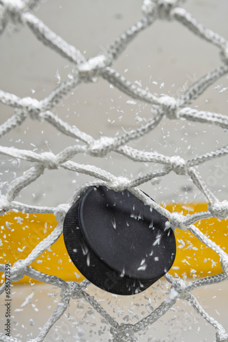 A close-up view of an Ice Hockey puck hitting the back of the goal net as shavings fly by, viewed from the front. Scoring a goal in ice hockey.