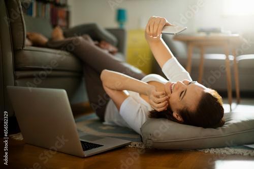 Young woman using her smartphone on the floor of her living room at home