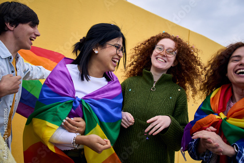 Group excited young diverse people laughing yellow wall background. LGBT community enjoying gay pride day outdoors. Liberal people celebrating street party. Rainbow flags and friends of generation z. photo