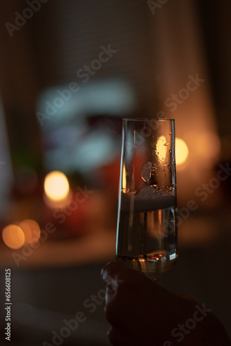 Close up shot of glass of champagne held by a hand indoors. Lit candles in the background.