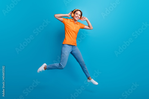 Fototapeta Naklejka Na Ścianę i Meble -  Full length photo of good mood ecstatic woman wear orange t-shirt jeans listen playlist in headphones isolated on blue color background