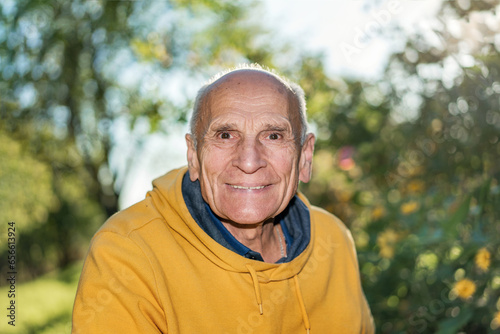 Fototapeta Naklejka Na Ścianę i Meble -  Wrinkled face of healthy happy smiling elderly male person in garden outdoors on green nature background and sunlight