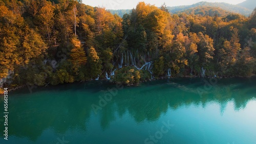 Turquoise water in a mountain forest lake with bright autumn trees. Aerial view of waterfall in golden woods. Clear aqua in reservoir.