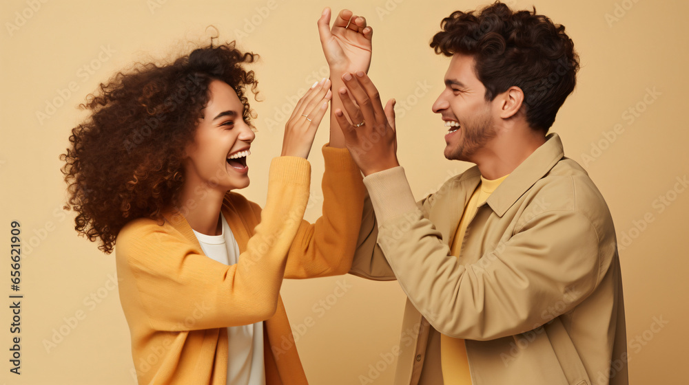 Side view of cheerful boyfriend and girlfriend giving high - five to each other and screaming over beige background. Excited young couple clapping hands and celebrating success - obrazy, fototapety, plakaty 