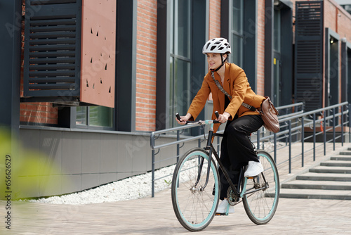 Photographie Young woman in formalwear and safety helmet sitting on bicycle and riding home f