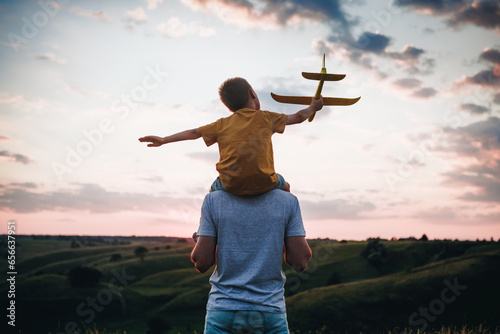 Dad and son playing together outdoors with yellow plane. Father and son launch a toy airplane at sunset. Happy family. Father's Day.