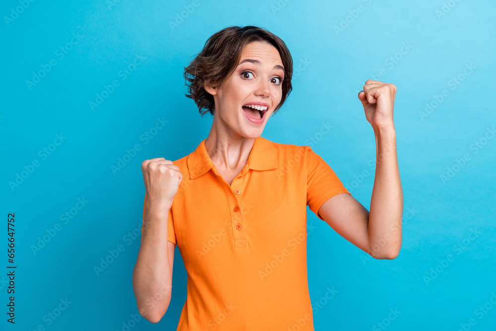 Photo of lucky excited girl dressed orange polo screaming eyes rising fists isolated blue color background Photo of lucky excited girl dressed orange polo screaming eyes rising fists isolated blue color background