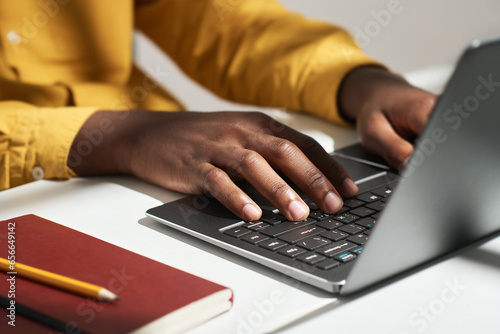 Hands of young male solopreneur pressing buttons of laptop keyboard while sitting by workplace in front of camera and entering data photo