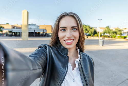 pretty young woman with blonde hair and blue eyes smiling while taking a selfie on the street