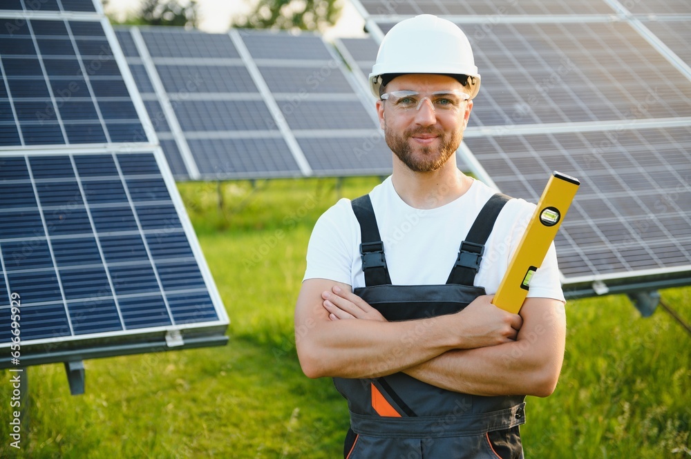 Side view of male worker installing solar modules and support structures of photovoltaic solar array. Electrician wearing safety helmet while working with solar panel. Concept of sun energy Side view of male worker installing solar modules and support structures of photovoltaic solar array. Electrician wearing safety helmet while working with solar panel. Concept of sun energy
