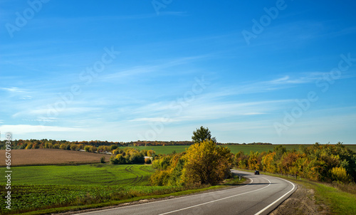 road along hilly field with green oil seed rape in foreground on a sunny autu...