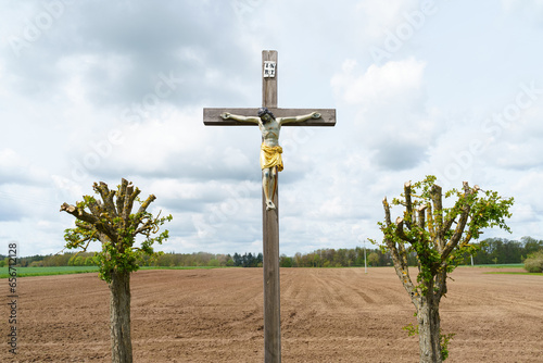 In front of a freshly plowed field stands the crucifixion of Jesus.