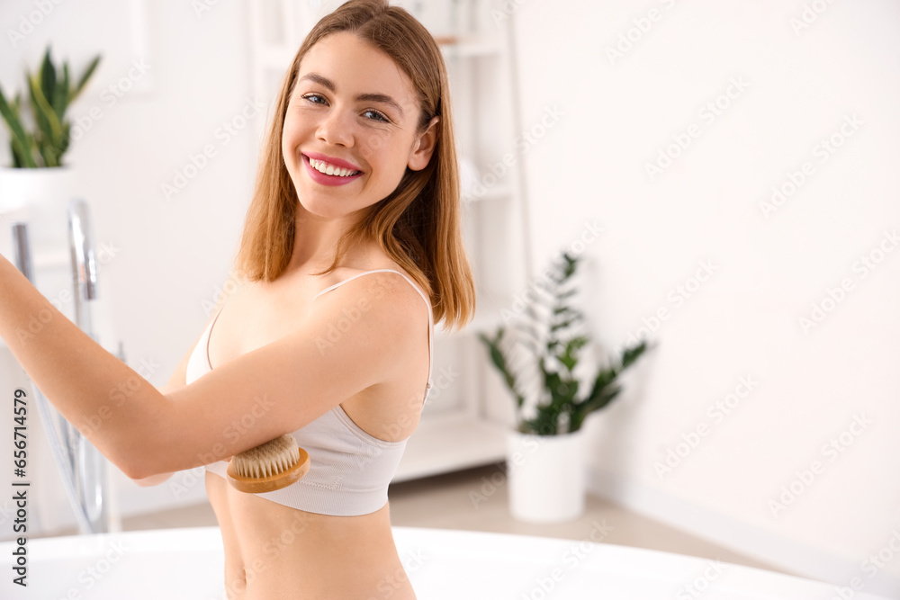 Young woman massaging her arm with anti-cellulite brush in bathroom Young woman massaging her arm with anti-cellulite brush in bathroom